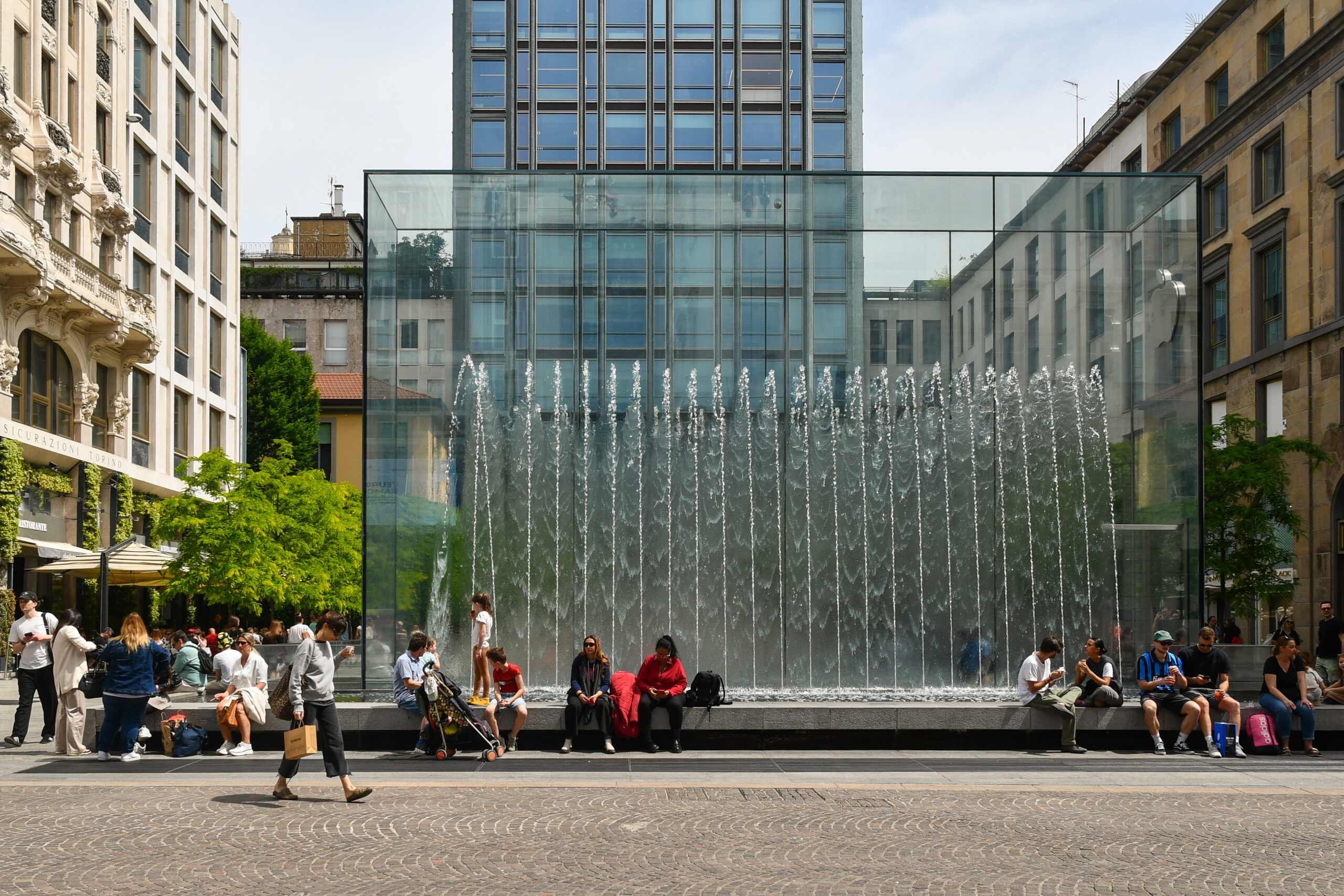 View of the central Piazza Liberty, with the striking glass fountain that serves as the entrance to the underground Apple Store, with tourists in spring, Milan, Lombardy, Italy
